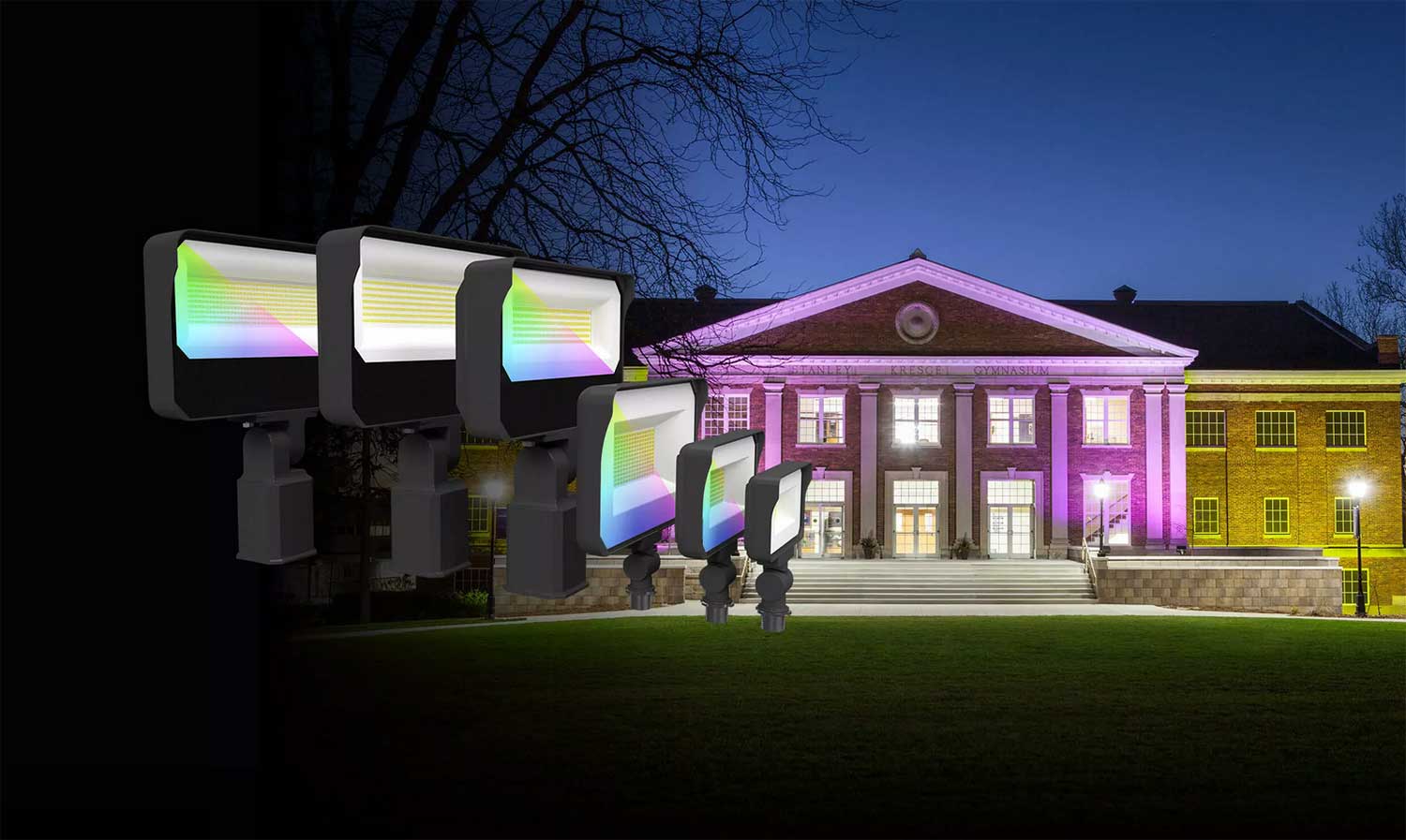 A row of colorful LED lights displayed in front of a brick building at dusk, with the building illuminated in purple.